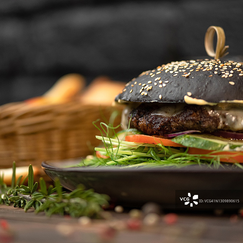 盘子里由黑麦面包、多汁肉和香草制成的黑色汉堡。快餐菜单概念。营养小吃或午餐。经典美式食物。柔焦特写镜头。侧视图图片素材