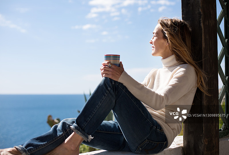 女人在俯瞰大海的露台上享受一杯咖啡图片素材