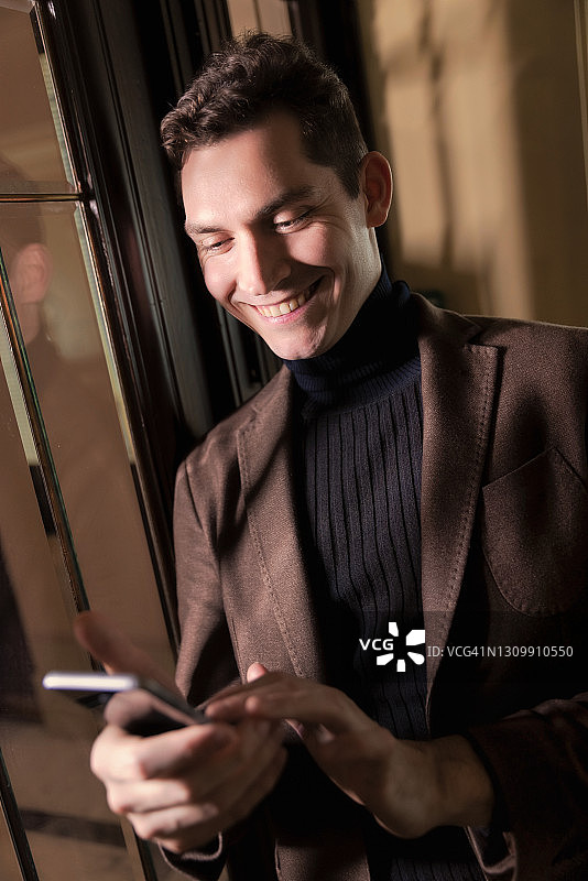 年轻男子在室内发短信并对着智能手机微笑图片素材