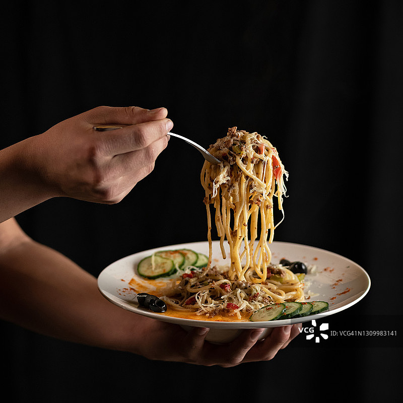 男人手持叉子，叉着大量意大利面，黑色背景，配沙拉的意面，近距离拍摄，经典意大利美食，方形构图图片素材