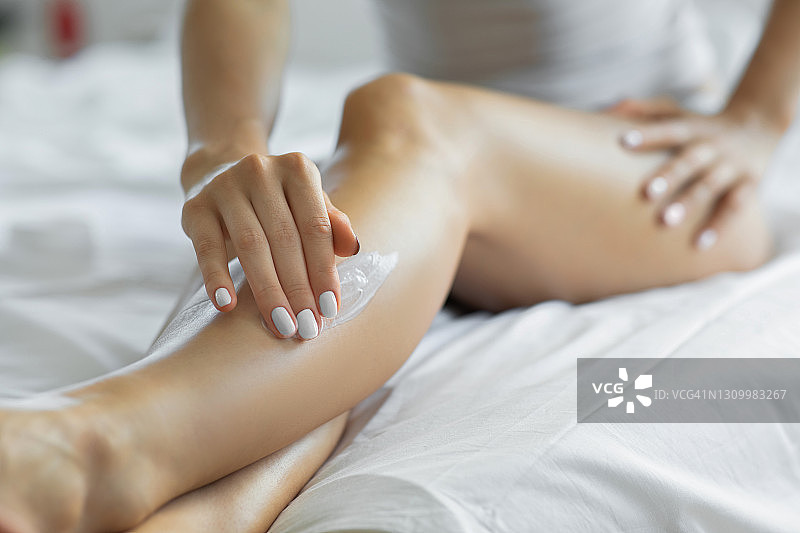 女人在卧室里往腿上涂抹润肤露图片素材