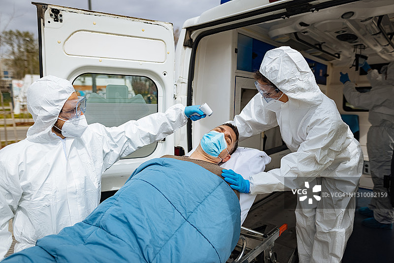 医护人员在救护车上为年长的COVID-19男性患者测量体温图片素材