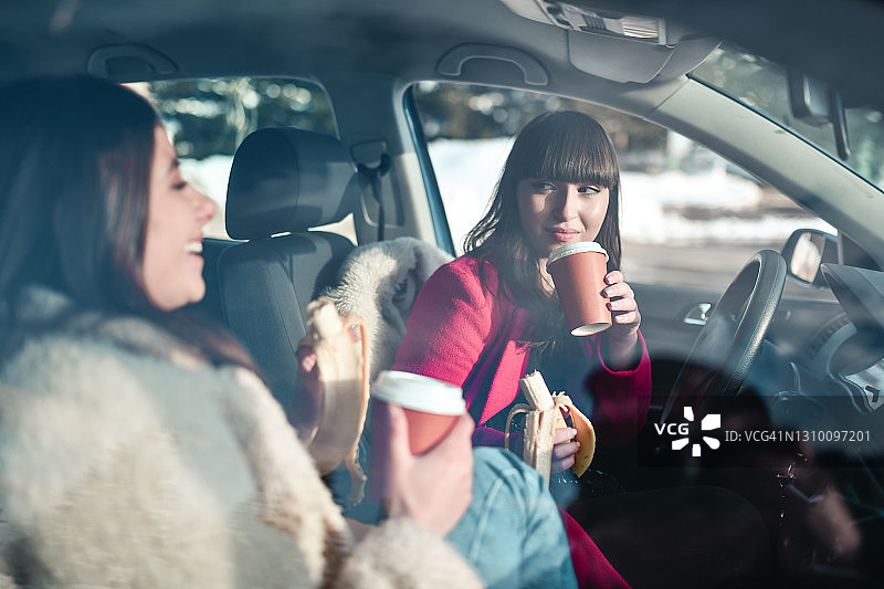 下雪天坐在车里享用香蕉和咖啡的可爱女人图片素材