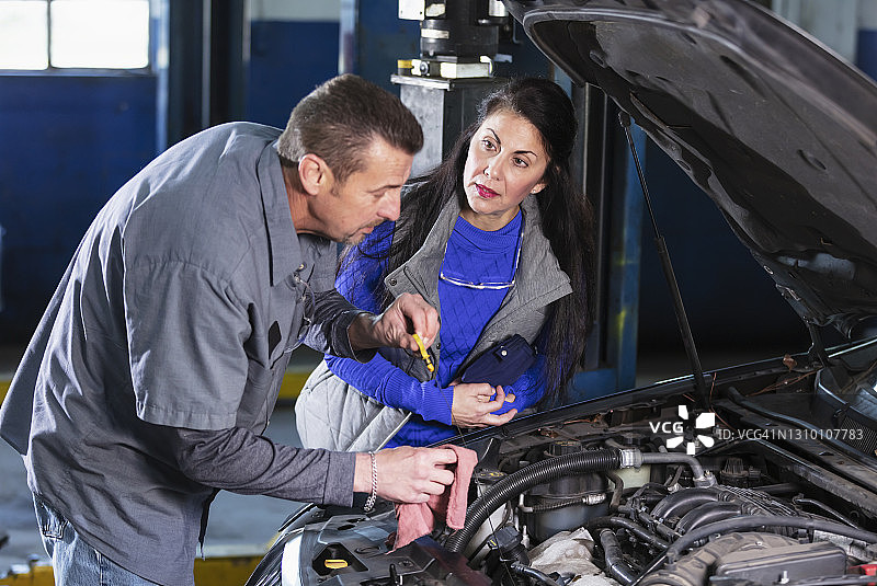汽车修理工检查油位，顾客在一旁观看图片素材