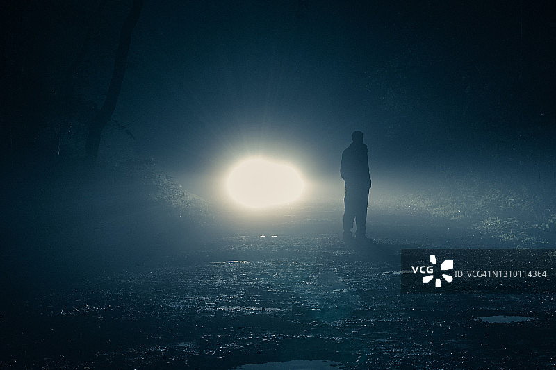 夜晚森林中，车头灯照亮雾气中的男人和树木图片素材