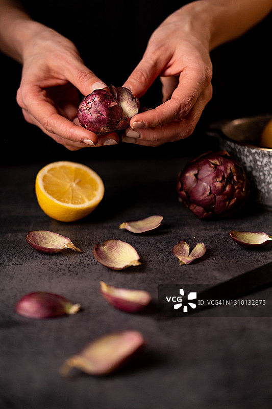 在黑色桌子上清洁成熟朝鲜蓟的手部特写。图片素材