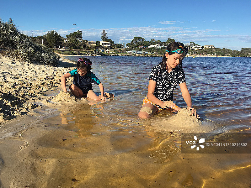 女孩们在海滩上堆沙堡图片素材
