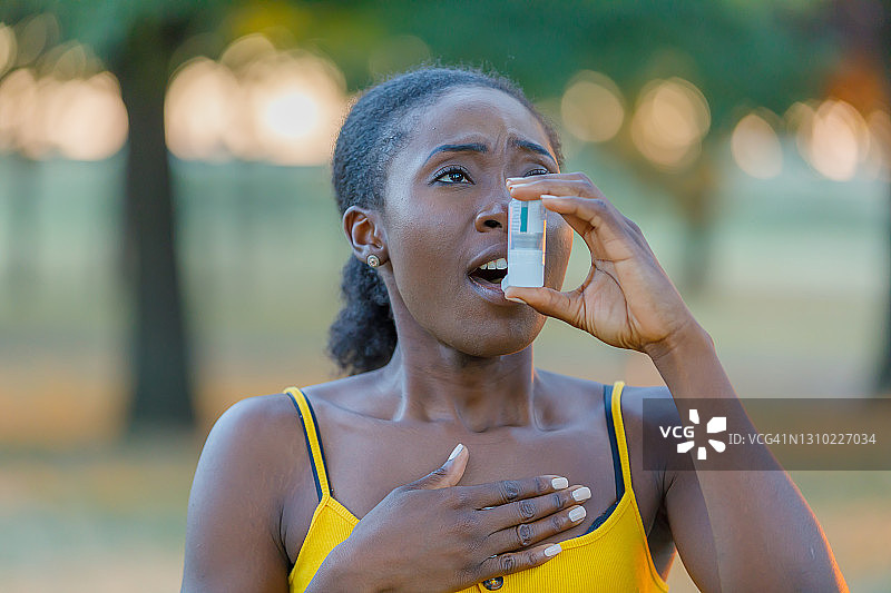过敏的非洲女人在公园里使用哮喘吸入器。图片素材