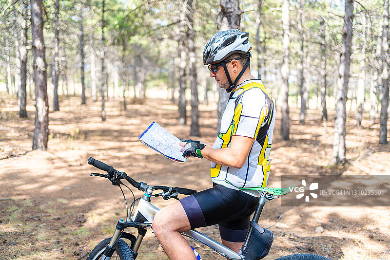 年轻专业自行车运动员在森林中查看地图图片素材