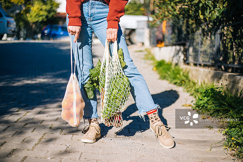 休闲年轻女人手拿可回收的网兜，里面装着各种水果和蔬菜图片素材