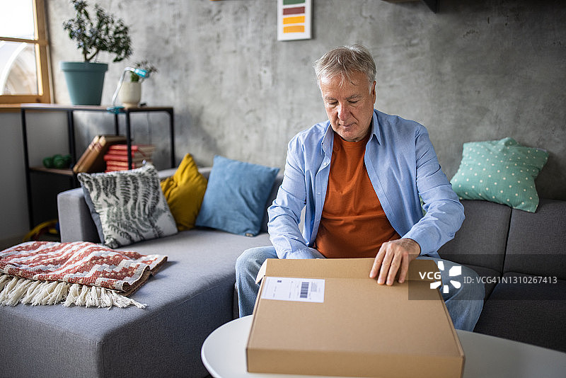 年长的男人在家里沙发上打开网上购买的纸箱图片素材
