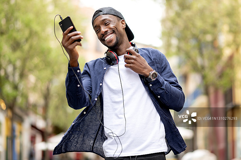 戴帽子和耳机看着手机微笑的非裔美国男人图片素材