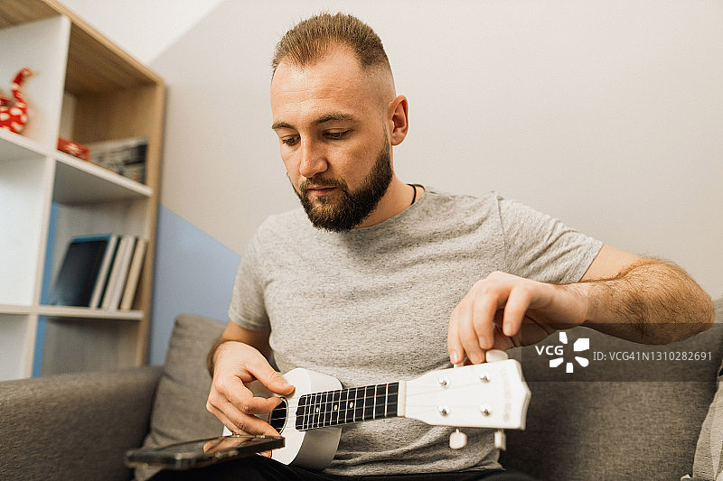 年轻人在家使用智能手机调音尤克里里图片素材