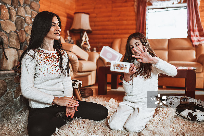 温馨小屋里，小女儿和母亲一起玩纸牌图片素材