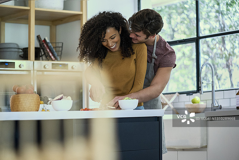 笑容满面的情侣在厨房柜台后相拥图片素材