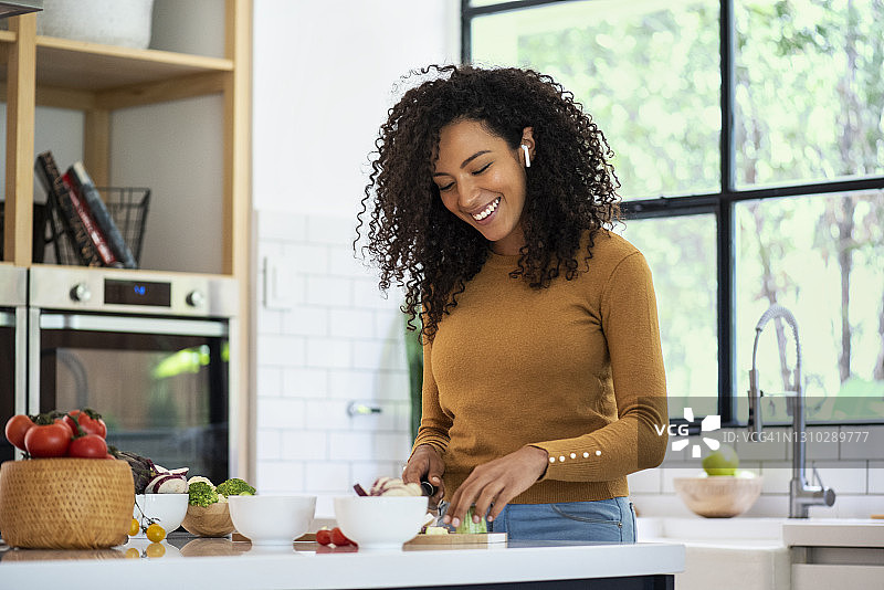 微笑的女人在厨房里听音乐和切菜图片素材
