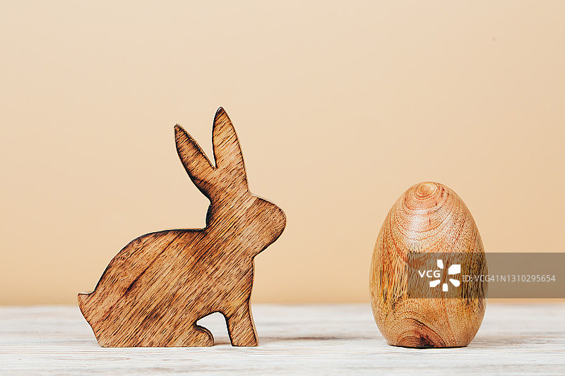米色背景上的木制兔子和木制蛋：生态复活节庆祝和春天的到来图片素材