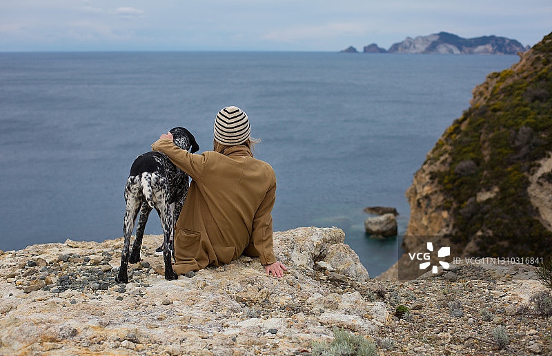 女人和她的狗坐在悬崖边，看着大海图片素材