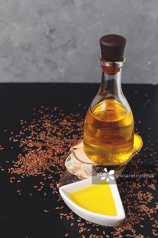 白色碗里的亚麻籽和玻璃瓶装亚麻籽油，在深灰色背景的木制砧板上图片素材