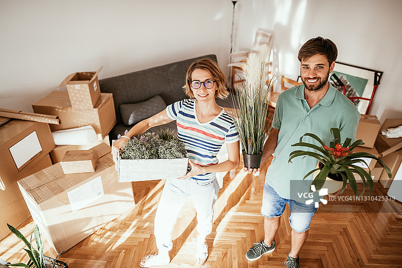 情侣搬进新租的公寓，搬运盆栽植物图片素材