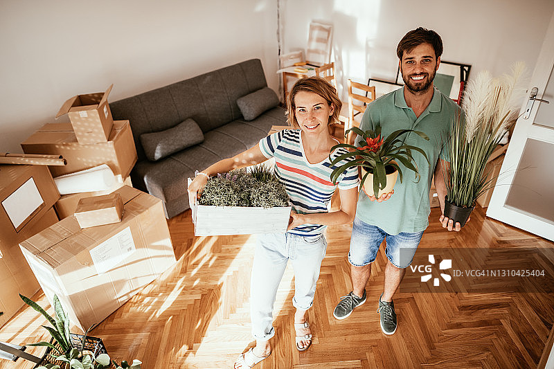 情侣搬进新租的公寓，搬运盆栽植物图片素材