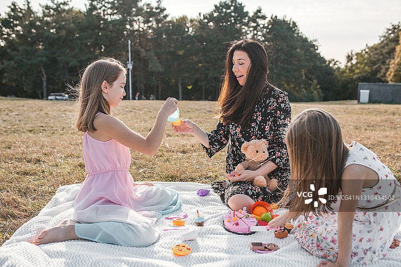 母亲和两个女儿及泰迪熊在公园里玩食物玩具图片素材