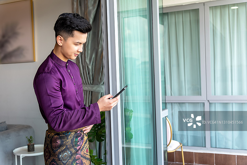 身穿马来西亚传统服饰的年轻男人正在看智能手机图片素材