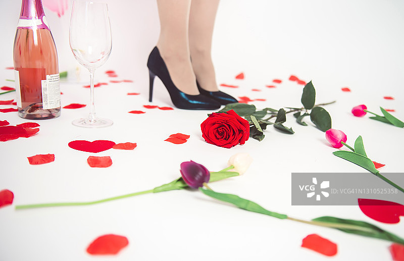 白色背景上，一瓶玫瑰酒和一个玻璃杯旁，穿着蓝色高跟鞋的女人图片素材