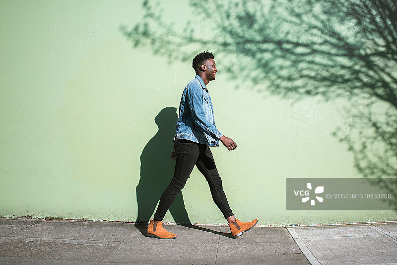 快乐的成年男子在阳光明媚的城市街道人行道上行走图片素材