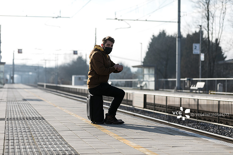 戴着防护面罩、拖着行李箱的孤独男人在火车站等火车图片素材