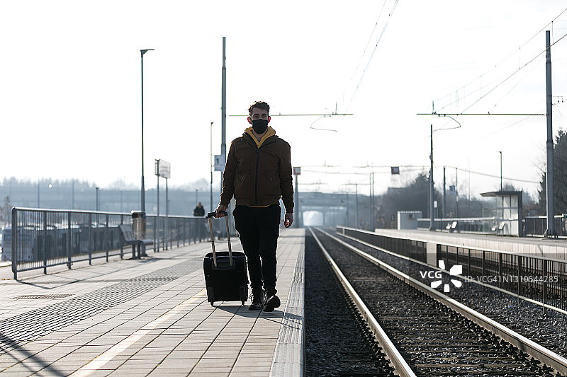 戴着防护口罩，正在等火车的白人男性图片素材