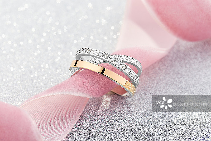 镶嵌白色宝石的金银戒指与粉色丝带图片素材