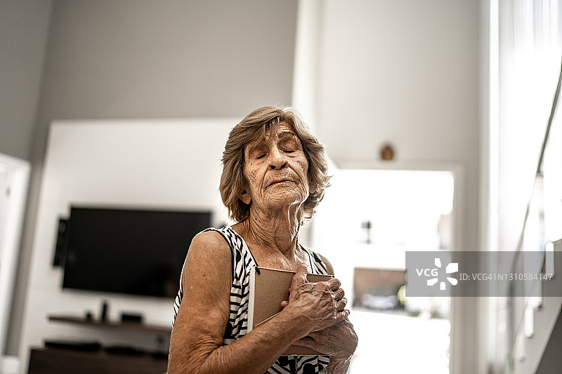 在家拥抱相框的悲伤老年妇女图片素材