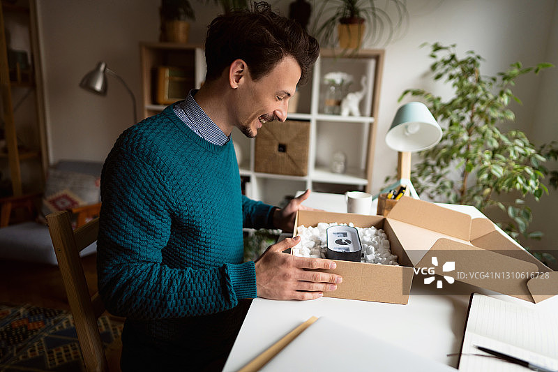 快乐的年轻男顾客在家打开送货包裹的侧面照图片素材