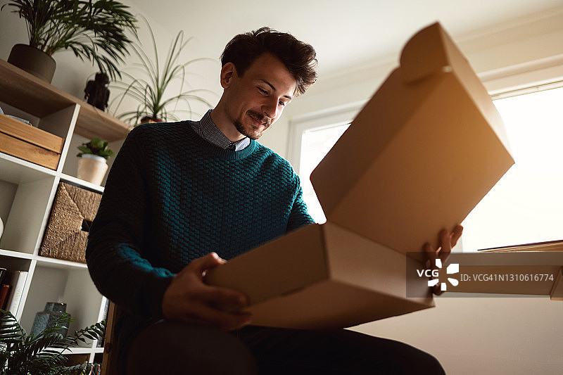 在家打开快递包裹的微笑男人图片素材