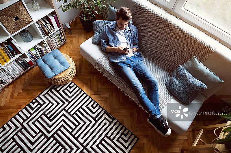 英俊男人躺在沙发上使用智能手机的高角度照片图片素材
