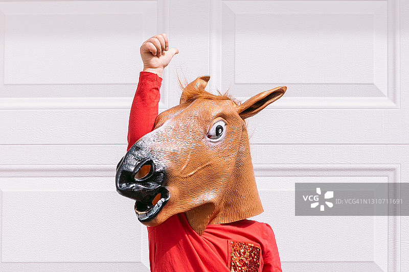 戴着马头乳胶面具的小男孩在车库白门前，兴奋地举起拳头图片素材