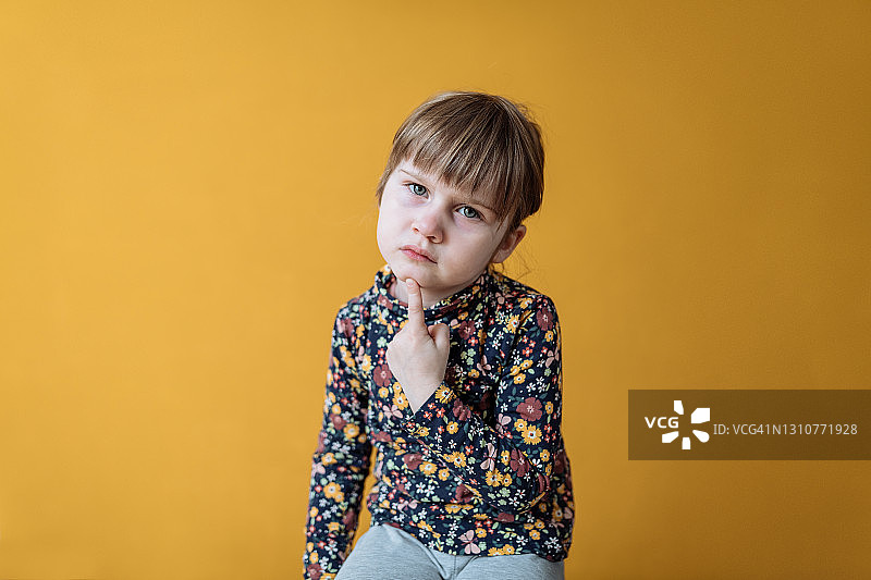 工作室沉思四岁女孩黄色背景肖像图片素材
