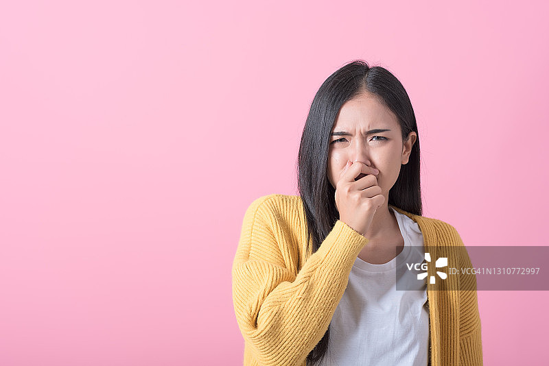 年轻女子因难闻的气味捂住鼻子，粉色背景图片素材