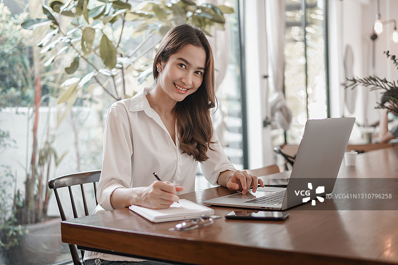 坐在桌旁用笔在笔记本上书写的女人图片素材