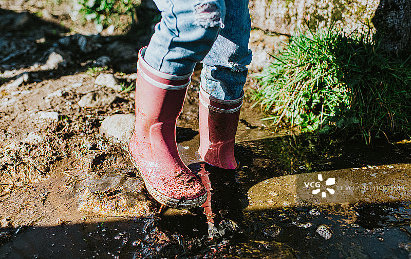 穿着粉色雨靴，在泥泞水坑中蹒跚而行的孩子图片素材