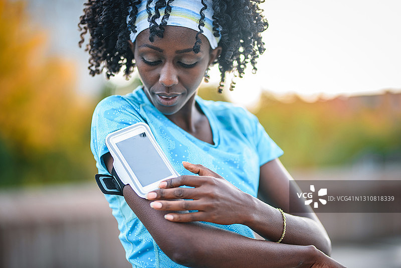跑步前在智能手机上选择音乐的黑人女运动员图片素材