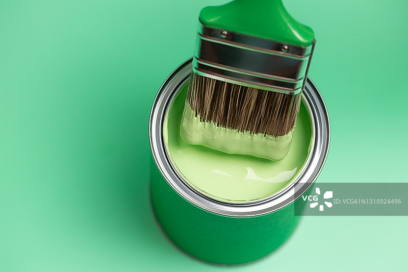 绿色的油漆从画笔刷毛滴入带有颜料的罐中，背景为柔和的翠绿色。家居维修概念。正面和特写图片素材