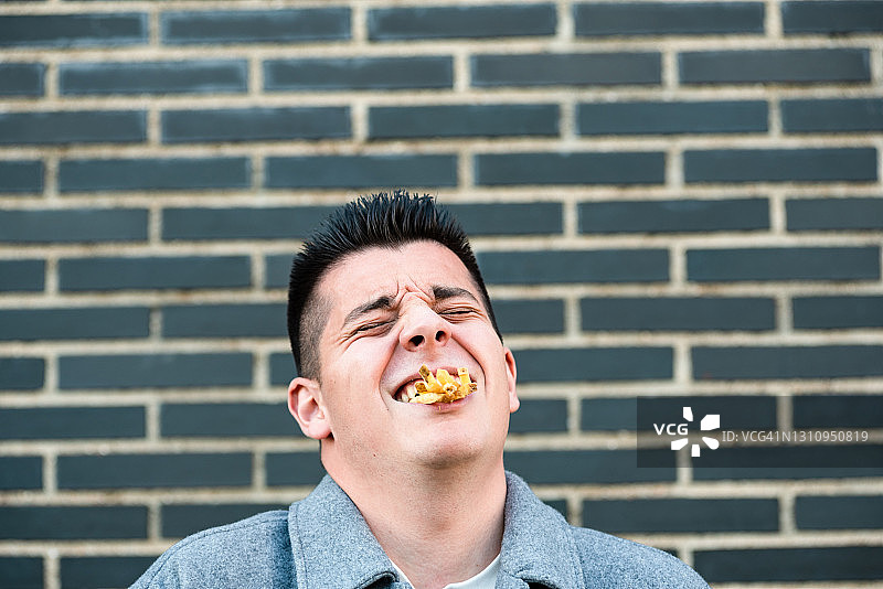嘴里含着很多薯片大笑的年轻男人图片素材