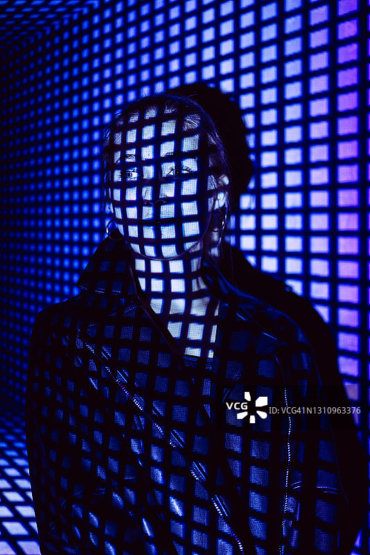 自信的年轻女性站在投影屏幕前的肖像。她被方形霓虹灯代码照亮。图片素材
