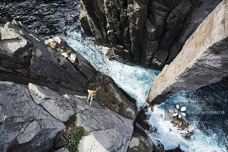 女子攀岩者从海边悬崖速降至图腾柱底部，下方海浪拍打图片素材