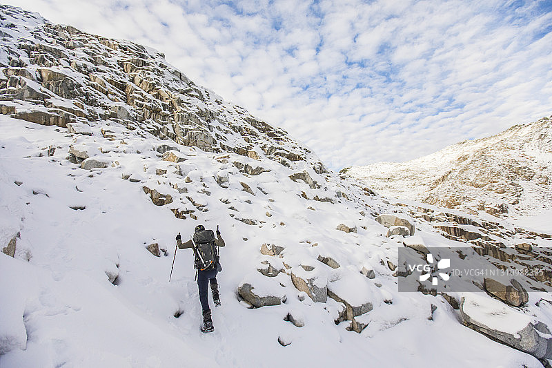 背包客徒步登上积雪的岩石斜坡的背影图片素材