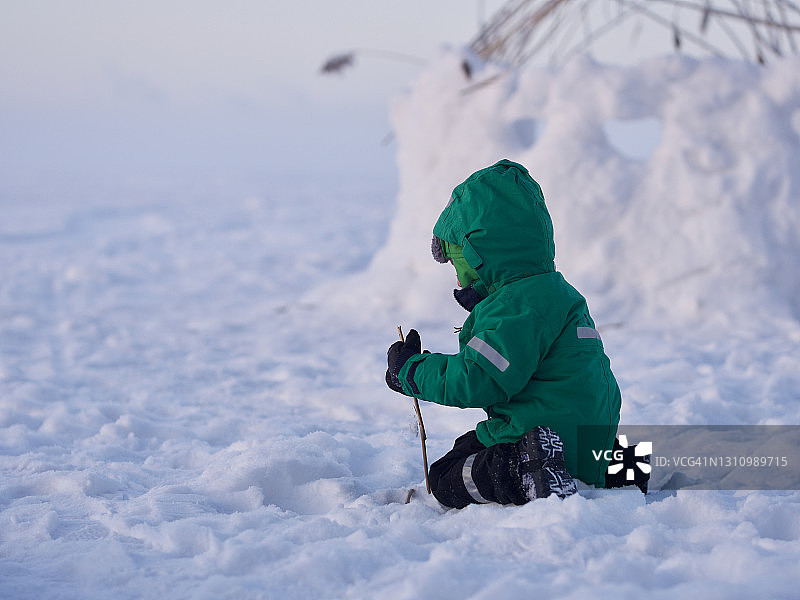 寒冷的冬日，小男孩在雪地里玩树枝图片素材