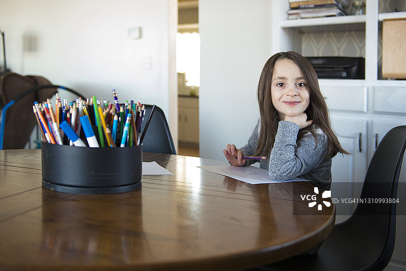 坐在桌旁用纸和铅笔画画的小女孩图片素材