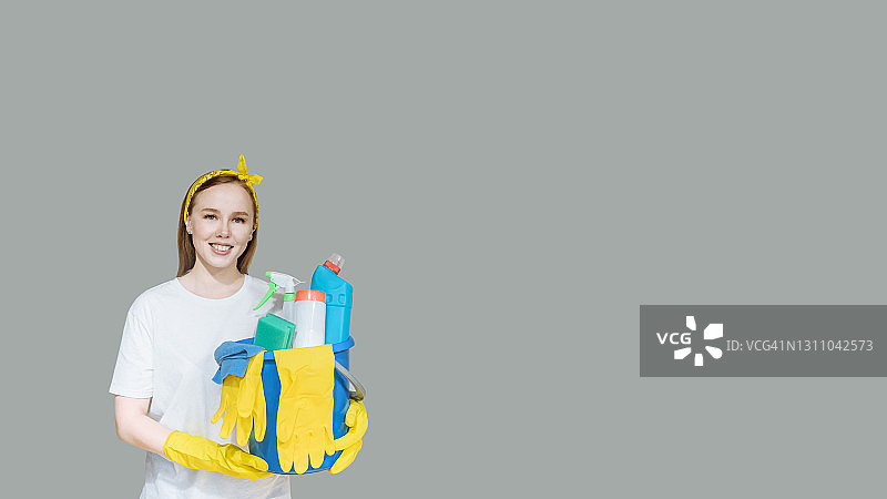 清洁，干净。年轻微笑的女佣拿着家用清洁产品。灰色背景演播室复制空间banner图片素材